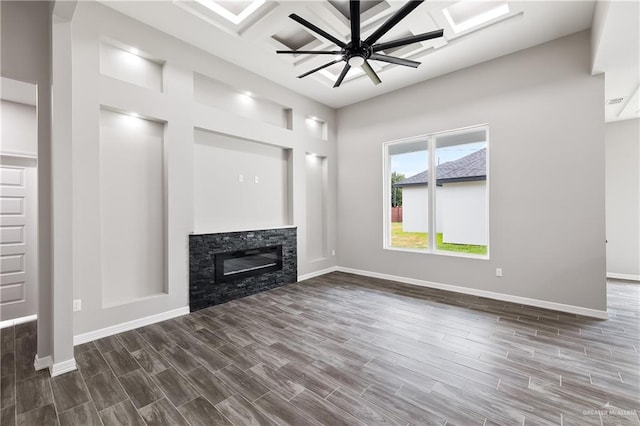 unfurnished living room featuring a stone fireplace, ceiling fan, coffered ceiling, and dark hardwood / wood-style floors