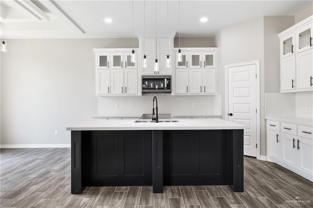 kitchen featuring sink, white cabinetry, hanging light fixtures, and an island with sink