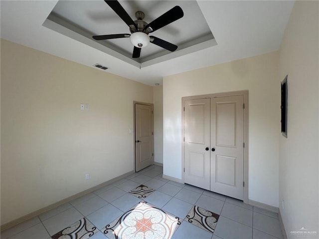 unfurnished bedroom with a raised ceiling, ceiling fan, a closet, and light tile patterned floors