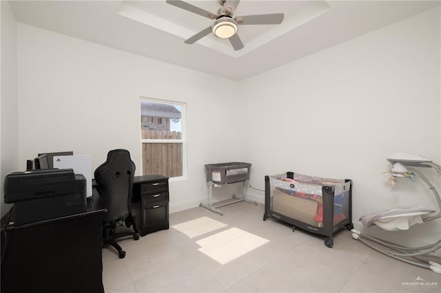 office space with a tray ceiling, ceiling fan, and baseboards