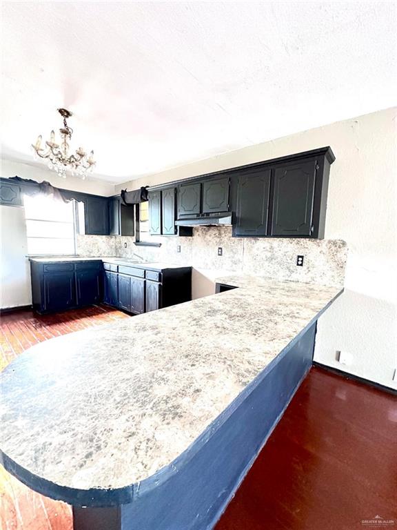 kitchen featuring hanging light fixtures, dark hardwood / wood-style floors, backsplash, kitchen peninsula, and a chandelier