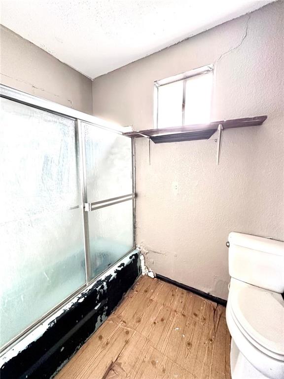 bathroom with shower / bath combination with glass door, wood-type flooring, a textured ceiling, and toilet