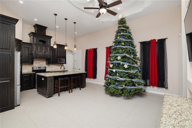 kitchen with dark brown cabinetry, a tray ceiling, stainless steel appliances, range hood, and a kitchen island with sink