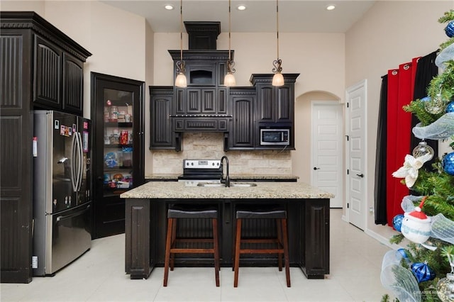 kitchen featuring stainless steel appliances, range hood, sink, and a center island with sink