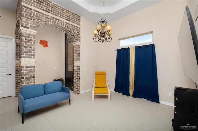 sitting room featuring tile patterned flooring, a raised ceiling, a chandelier, and brick wall