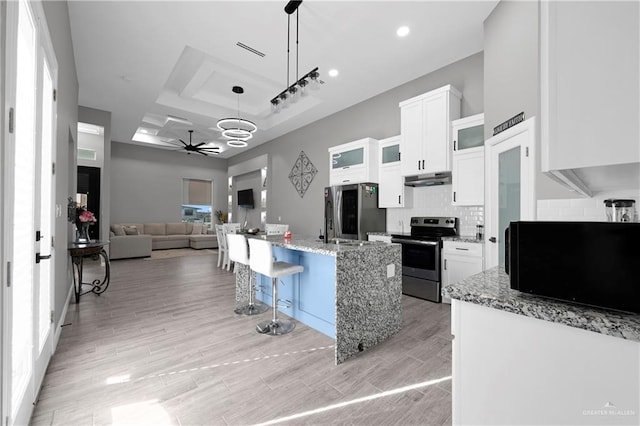 kitchen featuring light stone countertops, pendant lighting, white cabinets, appliances with stainless steel finishes, and a kitchen island with sink