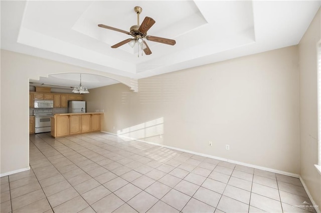 unfurnished living room with ceiling fan with notable chandelier, a raised ceiling, and light tile patterned floors