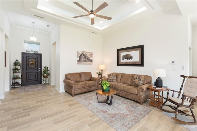 living room with a tray ceiling, ceiling fan, a high ceiling, and light wood-type flooring