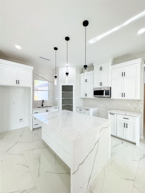 kitchen featuring sink, white cabinetry, light stone counters, a center island, and hanging light fixtures