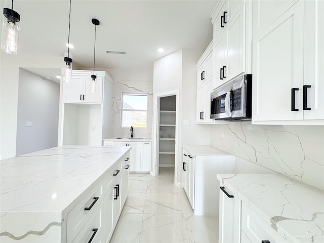 kitchen with white cabinetry, sink, decorative light fixtures, and light stone counters