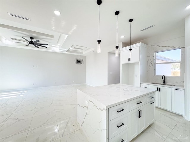 kitchen featuring white cabinetry, a center island, sink, and light stone counters