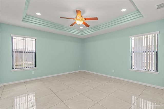 empty room with a raised ceiling, a wealth of natural light, ceiling fan, and light tile patterned floors