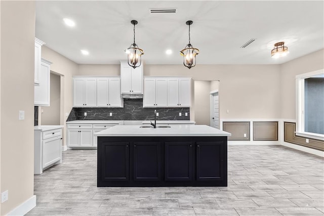 kitchen featuring decorative light fixtures, white cabinetry, a kitchen island with sink, and sink