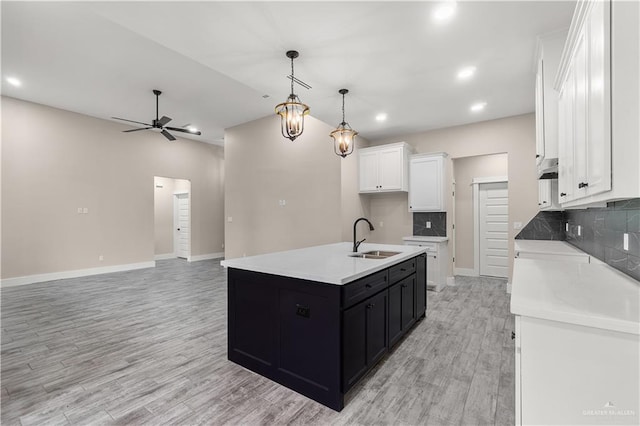 kitchen featuring a kitchen island with sink, sink, hanging light fixtures, ceiling fan, and white cabinetry