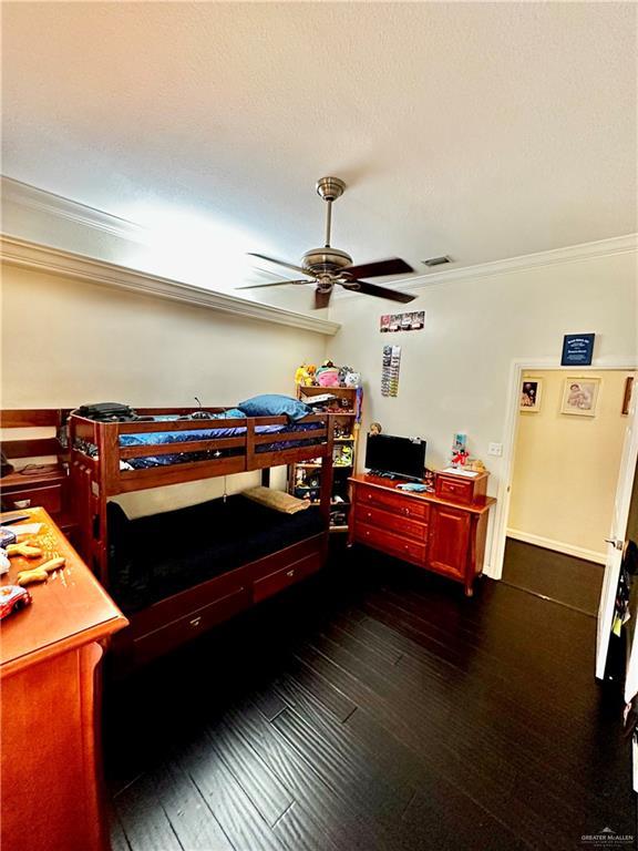 bedroom with visible vents, a ceiling fan, ornamental molding, and dark wood-style floors