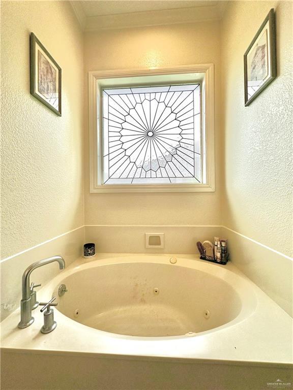 full bathroom with a tub with jets, a wealth of natural light, crown molding, and a textured wall