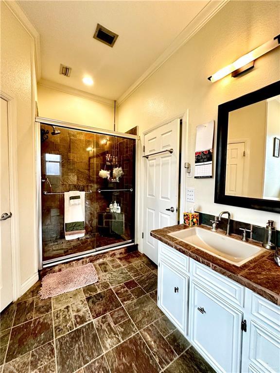 bathroom featuring vanity, visible vents, a stall shower, and ornamental molding