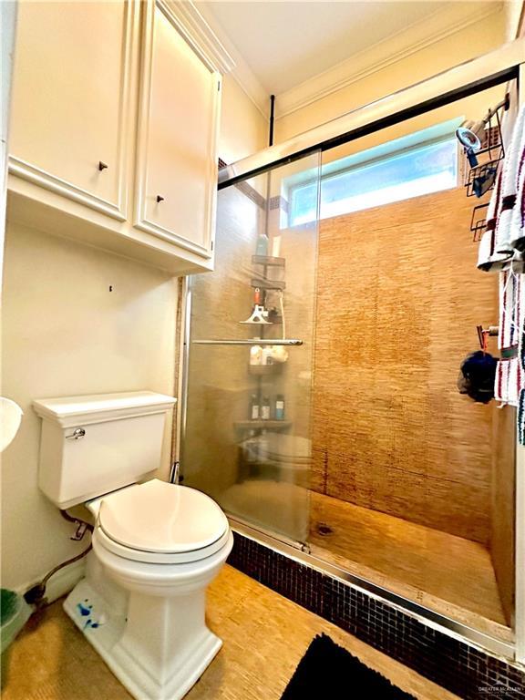 bathroom featuring toilet, a tile shower, and ornamental molding
