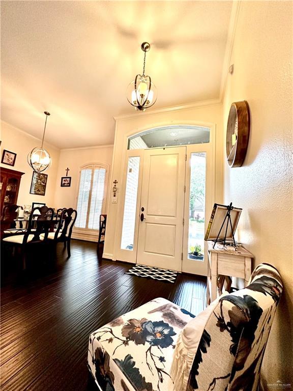 foyer entrance with dark wood-style flooring, ornamental molding, and a notable chandelier