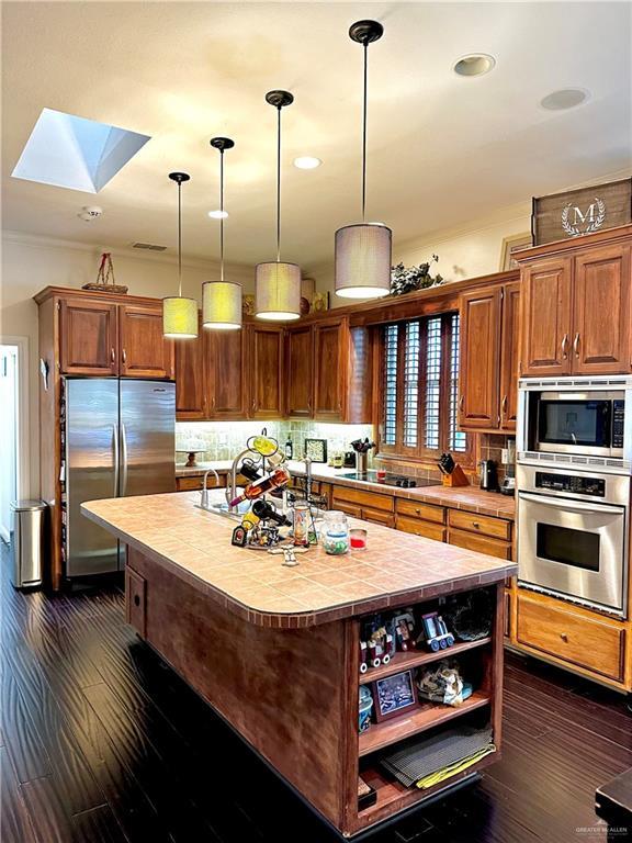 kitchen featuring a skylight, stainless steel appliances, open shelves, dark wood-style flooring, and tile counters