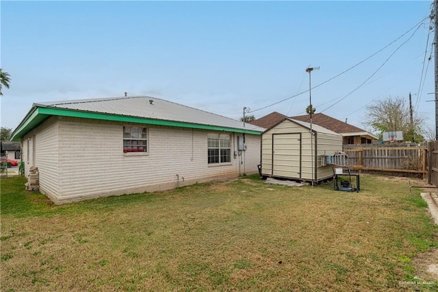 back of property with a storage shed, metal roof, an outbuilding, fence, and a yard