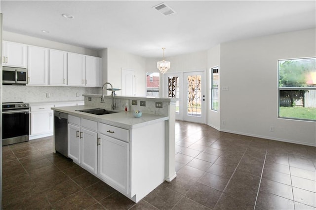 kitchen featuring stainless steel appliances, sink, white cabinetry, hanging light fixtures, and an island with sink