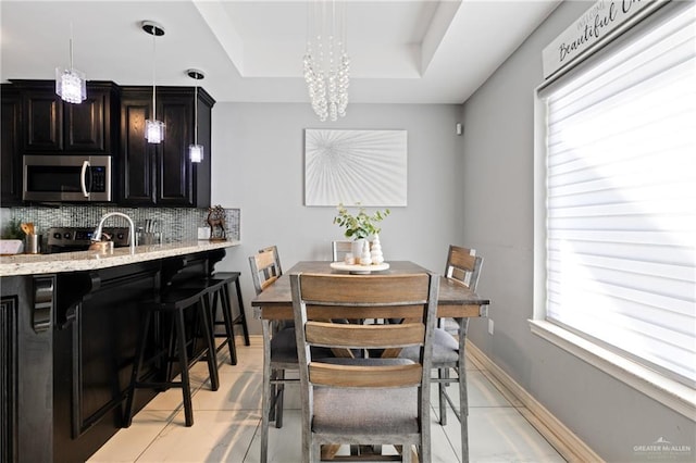 tiled dining area with a tray ceiling, an inviting chandelier, a wealth of natural light, and sink