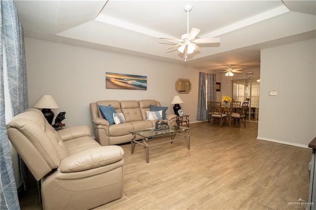 living room with a tray ceiling, ceiling fan, and light wood-type flooring