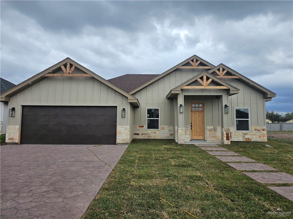 view of front of property with a front yard, stone siding, driveway, and an attached garage