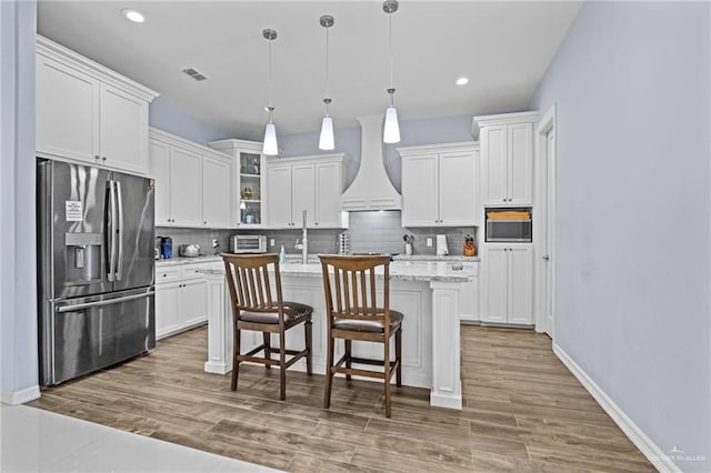 kitchen featuring white cabinetry, a kitchen island with sink, stainless steel appliances, and custom exhaust hood