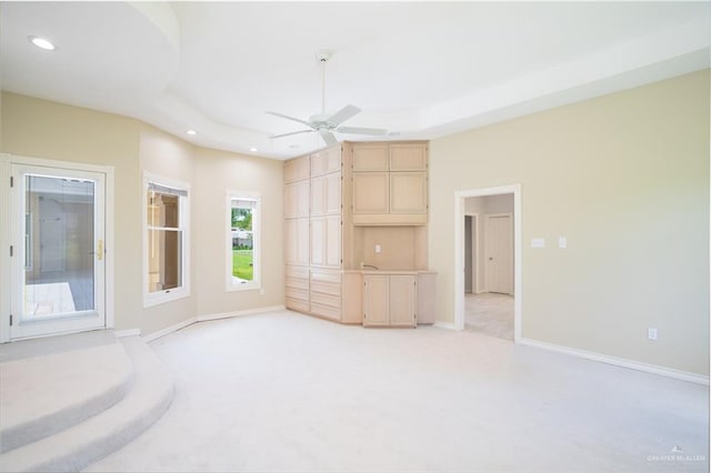 unfurnished living room with ceiling fan, light colored carpet, and a raised ceiling