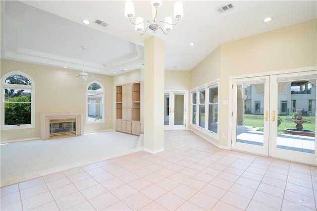 unfurnished living room featuring a raised ceiling, light colored carpet, french doors, and ceiling fan with notable chandelier