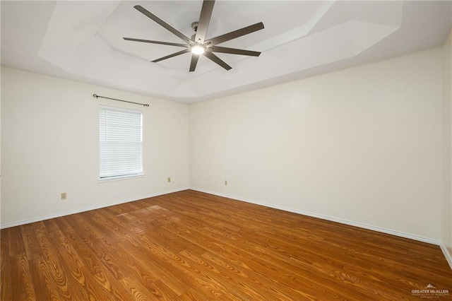 empty room with hardwood / wood-style flooring, a raised ceiling, and ceiling fan