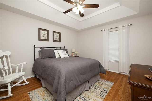 bedroom with dark hardwood / wood-style floors, ceiling fan, and a tray ceiling