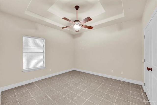 spare room with baseboards, a tray ceiling, and ceiling fan