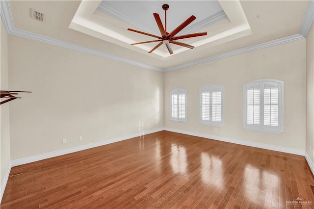 unfurnished room with a tray ceiling, visible vents, plenty of natural light, and wood finished floors