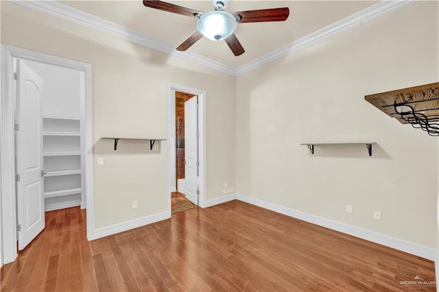 interior space with baseboards, ceiling fan, wood finished floors, a walk in closet, and crown molding