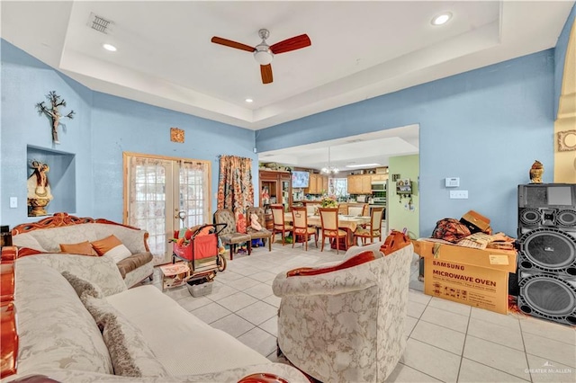 living room featuring a tray ceiling, french doors, light tile patterned floors, visible vents, and a ceiling fan