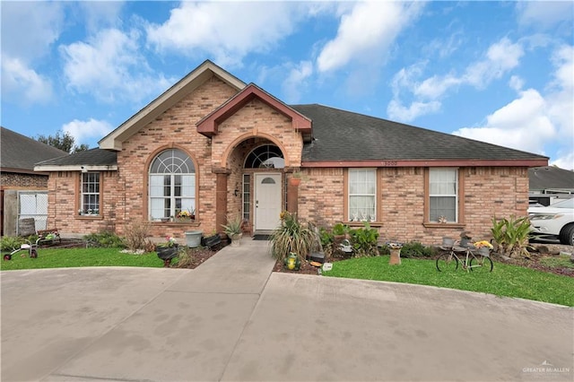 view of front of property with a front yard, brick siding, and roof with shingles