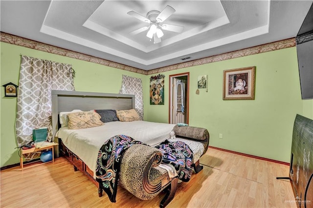 bedroom featuring a tray ceiling, light wood-type flooring, visible vents, and baseboards