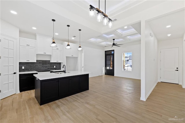 kitchen with an island with sink, white cabinetry, sink, backsplash, and coffered ceiling