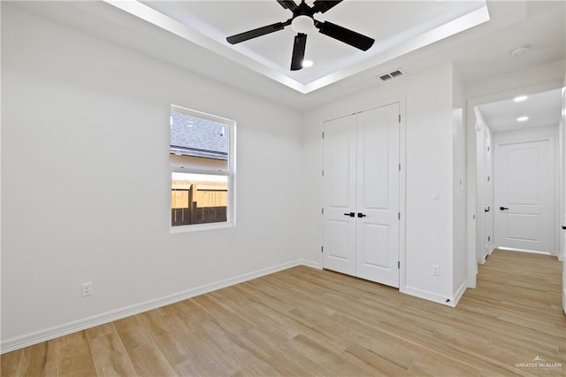 spare room featuring a tray ceiling, ceiling fan, and light hardwood / wood-style floors