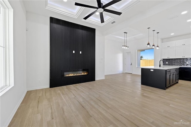 kitchen with a center island with sink, light hardwood / wood-style flooring, backsplash, decorative light fixtures, and white cabinets