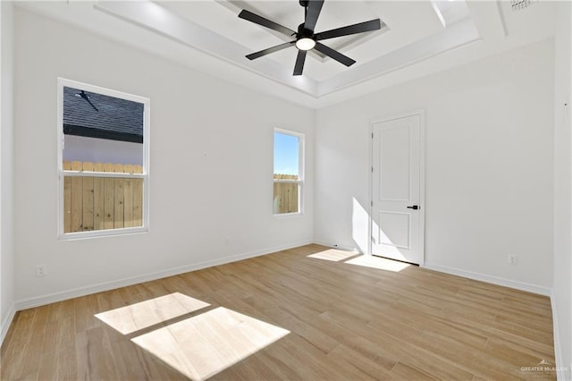 empty room with a tray ceiling, ceiling fan, and light hardwood / wood-style floors