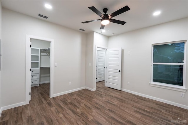 unfurnished bedroom featuring ceiling fan, a walk in closet, dark wood-type flooring, and a closet