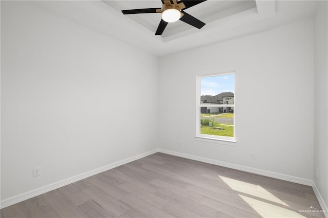 empty room with ceiling fan, a tray ceiling, and light hardwood / wood-style flooring