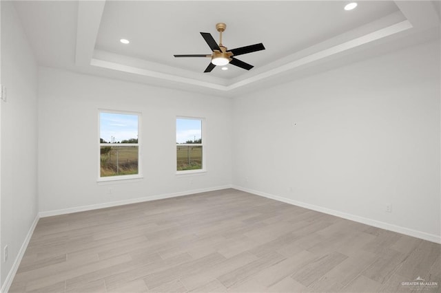 empty room featuring ceiling fan, light hardwood / wood-style floors, and a raised ceiling