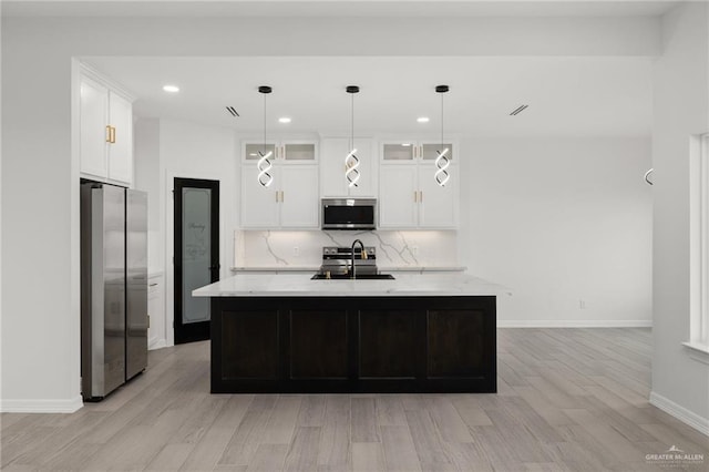 kitchen with decorative light fixtures, light hardwood / wood-style floors, sink, appliances with stainless steel finishes, and an island with sink