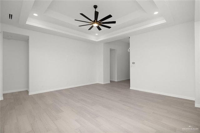 unfurnished room with ceiling fan, a tray ceiling, and light hardwood / wood-style flooring