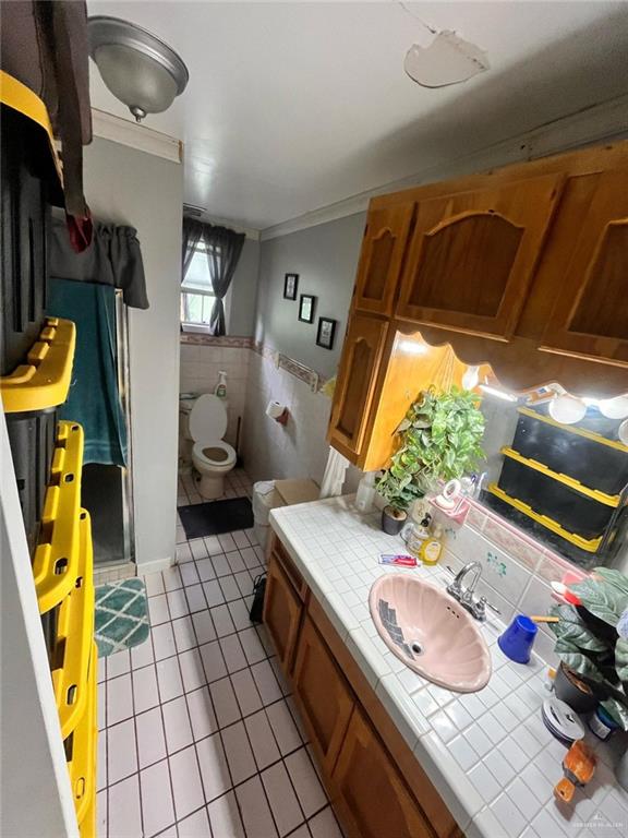 bathroom featuring tile patterned floors, a wainscoted wall, ornamental molding, a sink, and tile walls